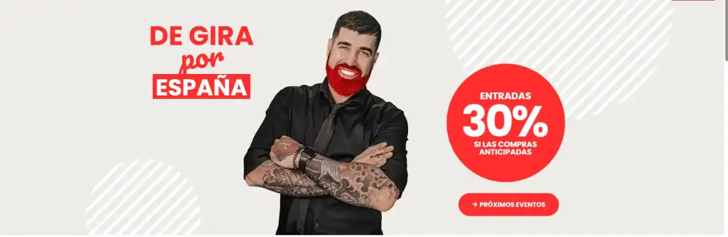 Un hombre con barba y tatuajes en los brazos está de pie delante de una pancarta que